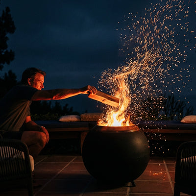 Person lighting a fire in a fire pit with sparks flying at night.